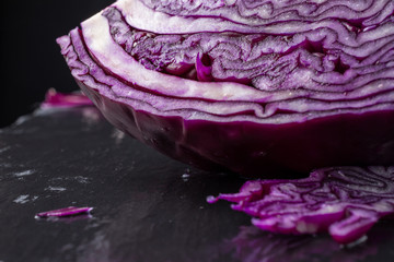 Obraz premium Close-up of red cabbage with pieces, selective focus, on wet black slate, black background, horizontal