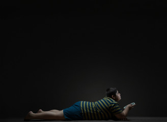 Young boy lying on the floor and changing channels with the TV remote. (Obesity) 
