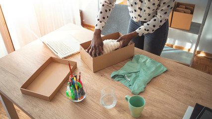 Organizing work in delivery business. Online shopping makes happy a lot of people. Woman packing item that she sells online. Young start up small business African-American owner packing cardboard box 