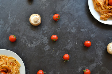 Pasta in a white plate. Pasta with tomato sauce, mushrooms with cherry tomatoes. Dark background. View from above. Free space for text.