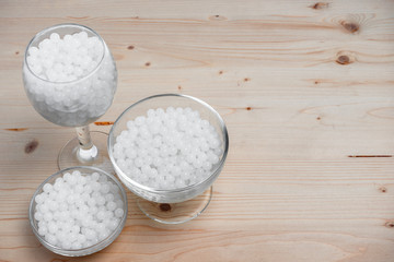 hydrogel white balls in glassware on wooden board. artificial moisture-absorbing material that contributes to accumulation and preservation of moisture. used for planting plants or children games