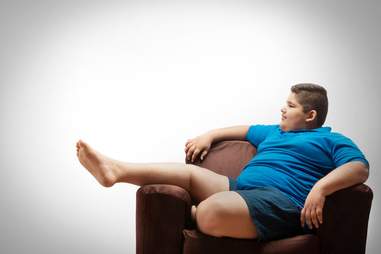Young boy relaxing on the sofa at home. (Obesity) 	
