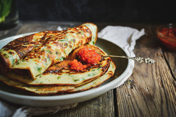 Thin pancakes with herbs. Salty Pancakes with green onions. Wood background. Vintage background. Delicious food for a bite to eat. Free space for text. Red sauce in a bowl. Vintage spoon with sauce.