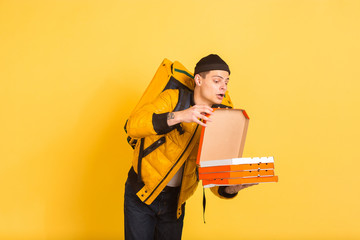 Proposing pizza for client. Emotions of caucasian deliveryman isolated on yellow background. Contacless delivery service during quarantine. Man delivers food during isolation. Safety. Hurrying up.