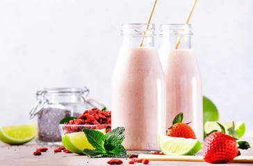 Healthy blended superfood drink. Organic diet smoothie with strawberry and goji berries, chia seeds and lime. Glass bottles with eco fendley straws. Gray background with copy space