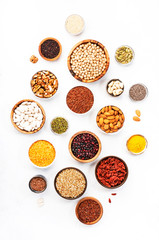Various superfoods, legumes, cereals, nuts, seeds in bowls on white background. Superfood as chia, spirulina, beans, goji berries, quinoa, turmeric, mung bean, buckwheat, lentils, flax seed