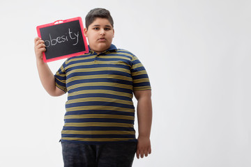 Young boy holding a small blackboard with obesity written on it. 	