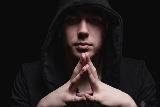 A man in a black hood on a black background, studio photography. The idea of mysticism, mystery, crime and deception