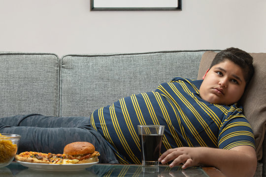 Young boy lying on the sofa with junk food kept on the table  at home. (Obesity) 	