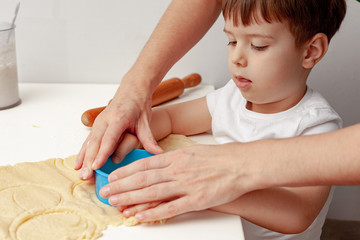 Happy family in the kitchen. Mother and son preparing the dough, bake cookies. Casual lifestyle in home interior, pretty child, holiday concept, rolling pin, coockie cutters and dough.