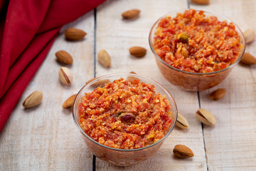 Fototapeta na wymiar Two bowls of gajar ka halwa kept on a wooden table with dry fruits scattered on it. 