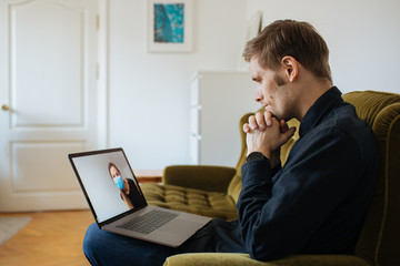 Caucasian man wearing casual shirt using computer for telemedicine. Online doctors in video call. Telehealth during pandemic. Video consult in the computer monitor doctor wear medical face mask