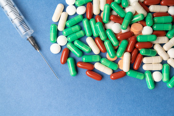 many multi-colored medical antiviral pills with syringe on blue background close-up