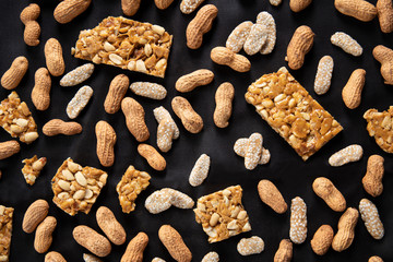 Groundnuts, chikki and rewari scattered on a black cloth.
