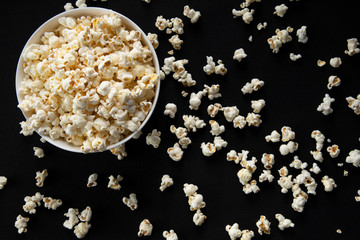 Obraz na płótnie Canvas Popcorns kept in a white bowl along with some scattered on a black background. 