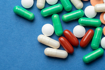 many multi-colored medical pills on blue background close-up
