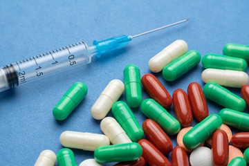many multi-colored medical antiviral pills with syringe on blue background close-up