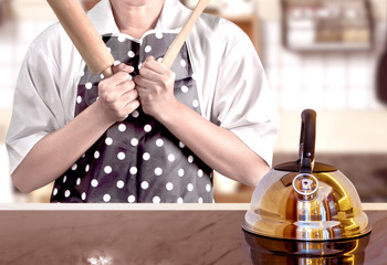 Woman with rolling pin and spatula standing with the kettle on the stove