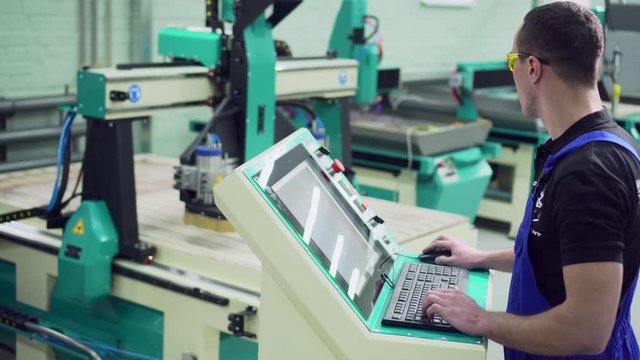 Cropped, male CNC machine operator sets the program on the control panel.