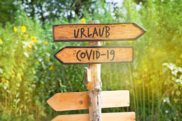 Wooden direction sign with the German words vacation and Covid-19 (Urlaub, Covid-19)