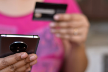 Shot of a woman looking at her smartphone and doing digital payment with her credit or debit card in her left hand. Concept - Digital finance and Fintech. 
Digital banking
