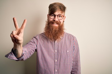 Fototapeta premium Handsome Irish redhead business man with beard wearing glasses over isolated background showing and pointing up with fingers number two while smiling confident and happy.