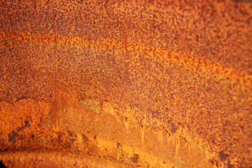 Old antique rounded metal surface is saturated red, orange, brown, yellow completely covered with thick layer of rust and corrosion in rays of setting sun. Stage aging metal.