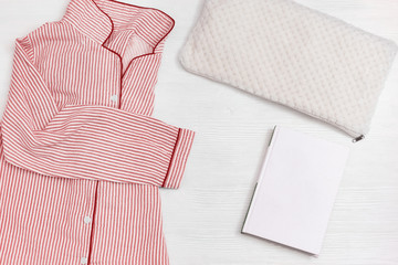 Sleepwear for slumber. Pink women pajama from cotton cloth with stripes, pillow, and book for reading before going to bed.  Top view. Flat lay.