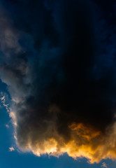 Fototapeta na wymiar Dark clouds drenched in sunset hues against a blue sky