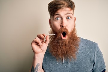 Irish redhead man with beard holding dental invisible aligner for tooth correction scared in shock...
