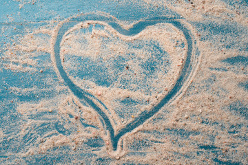 Golden beach sand with heart shape on a blue wood background. Summer travel love concept backdrop.