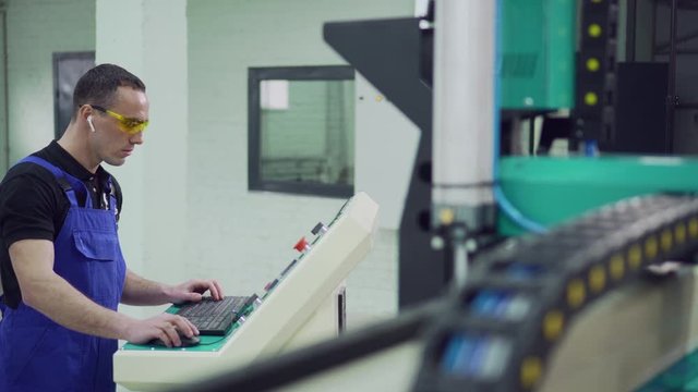 A male operator starts the CNC machine while standing at the control panel.