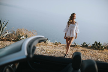 Young woman walking to cabriolet car at seaside