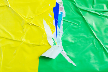 Yellow and green torn and crumpled placards on urban billboard with old ripped and peeling paper...