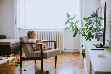 Little boy sitting on armchair and watching television in the room