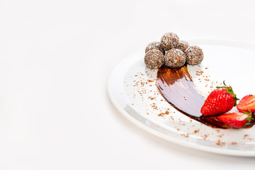 Energy balls or energy bites with oat, chocolate and coconut on white plate with strawberry and mint.