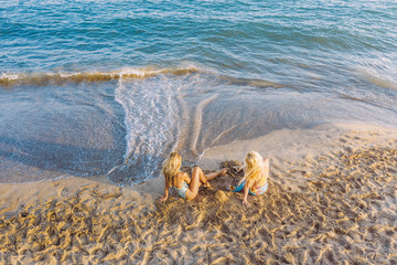 Fototapeta na wymiar two blond girls sitting on the shore of the beach