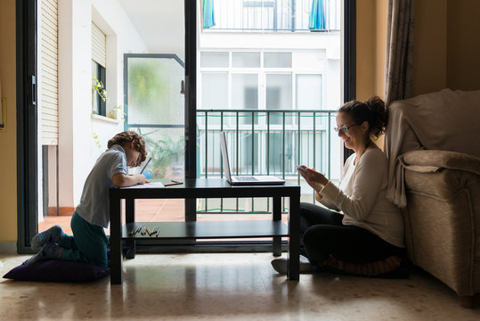 A woman and a child sitting on the floor doing work.