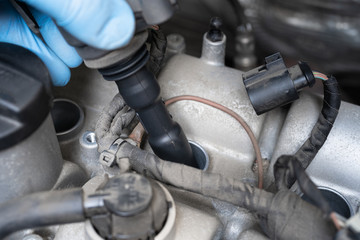Man in protective glove removing ignition coil in car engine bay. Mechanic repair or vehicle...