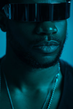 handsome african american man in futuristic sunglasses posing isolated on blue in blue light