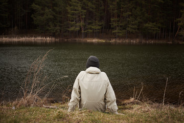 man sits and looks at the landscape from the forest in front of the pond