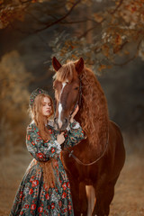 Fototapeta na wymiar Beautiful long-haired blonde young woman in national russian style with red Vladimir draft horse in autumn forest