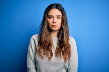 Fototapeta premium Young beautiful brunette woman wearing casual sweater standing over blue background with serious expression on face. Simple and natural looking at the camera.