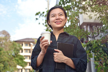 Cheerful  girl standing outdoor holding paper cup with coffee