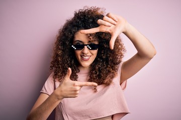 Young beautiful woman with curly hair and piercing wearing funny thug life sunglasses smiling...