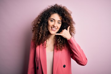 Young beautiful businesswoman with curly hair and piercing wearing elegant jacket smiling doing phone gesture with hand and fingers like talking on the telephone. Communicating concepts.