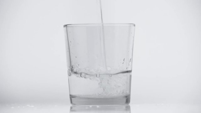 refreshing water pouring in glass on white