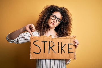 Young beautiful activist woman with curly hair and piercing protesting in strike holding poster...