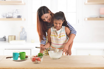 Mother and daughter kneading dough together in kitchen
