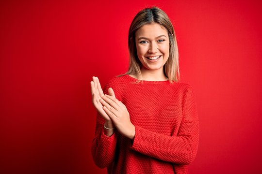 Young beautiful blonde woman wearing casual sweater over red isolated background clapping and applauding happy and joyful, smiling proud hands together